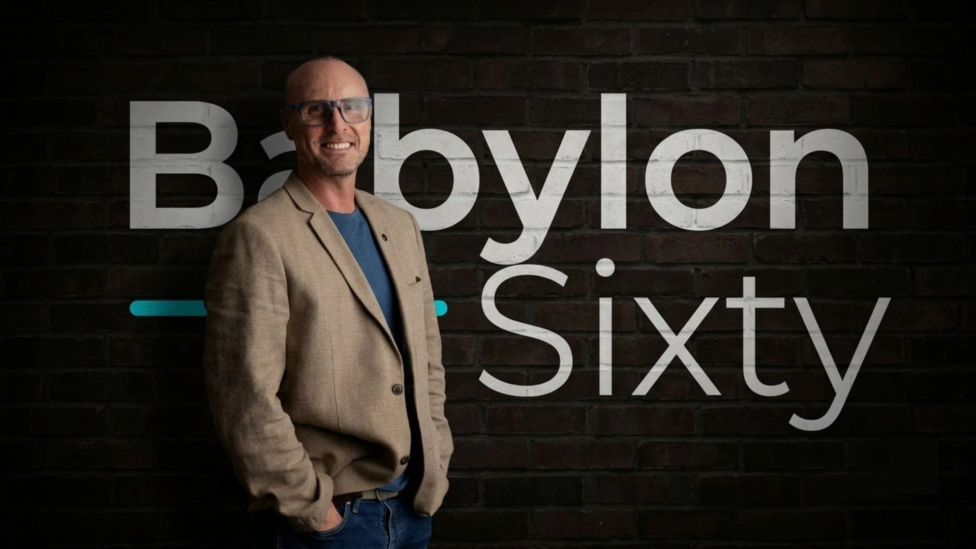 Darren Hopper standing in front of a brick wall painted with the BabylonSixty logo